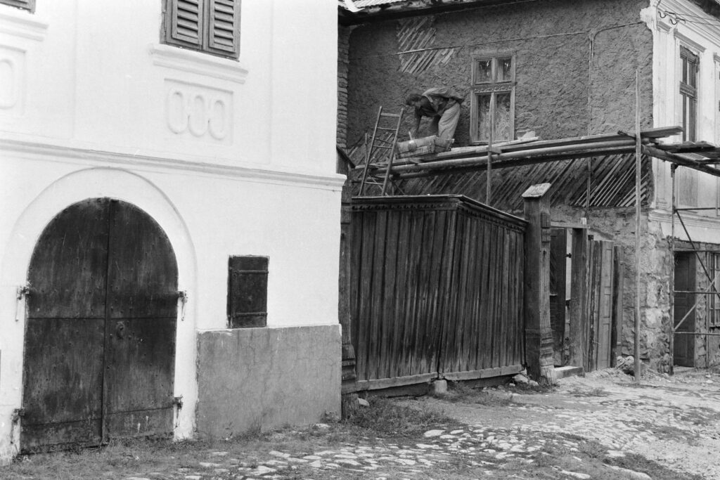 Fekete-fehér fénykép 1987-ből: torockói ház állványzattal, omló vakolatú homlokzattal, mellette fehér kőház boltíves kapuval