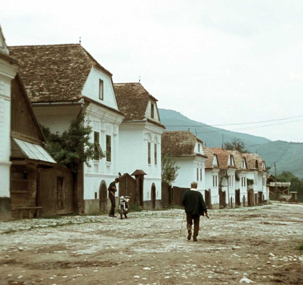 Színes fénykép 1965-ből: torockói utcasor fehér, oromzatos kőházakkal, zsindelytetővel, földúton sétáló férfi